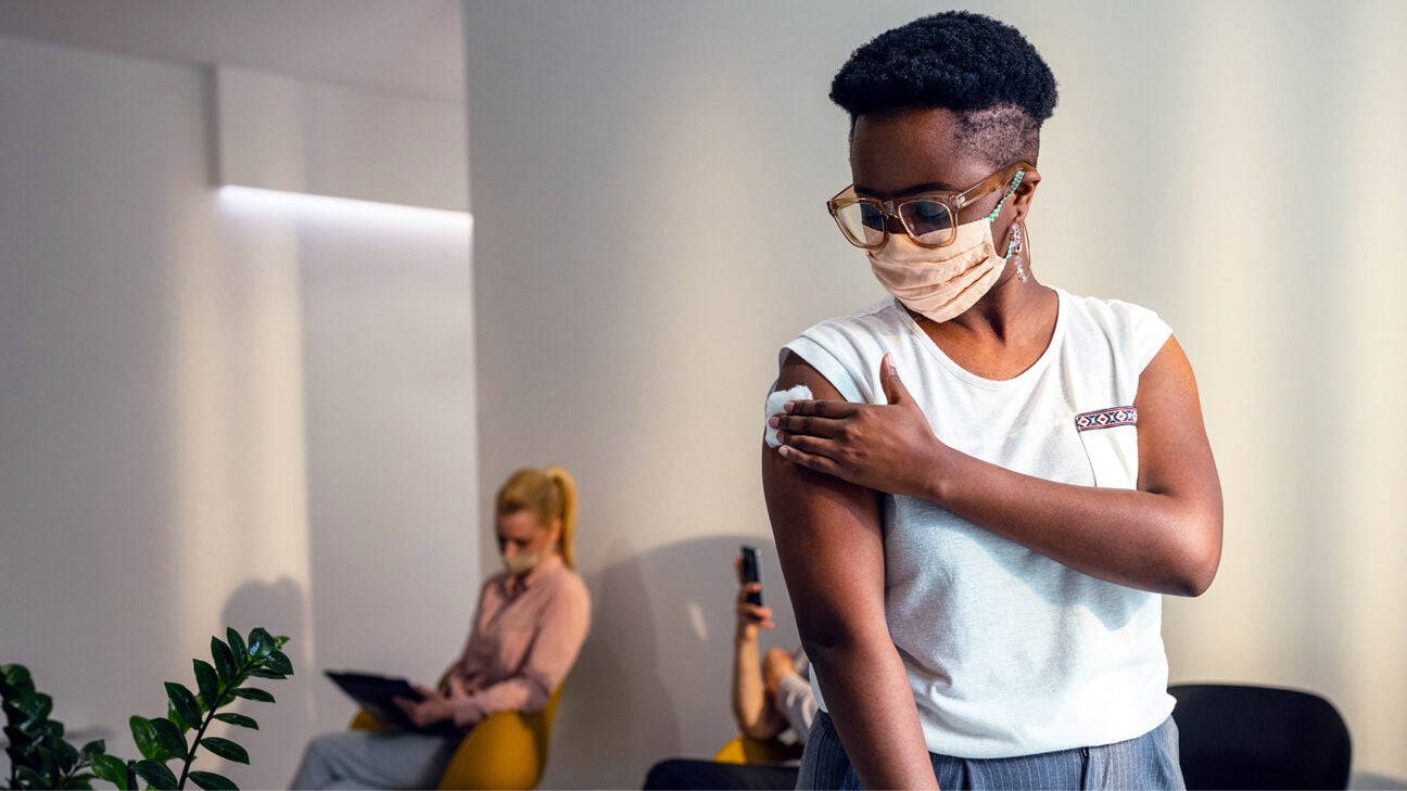 Someone in a waiting room, holding a piece of medical gauze to their arm after receiving a vaccine.