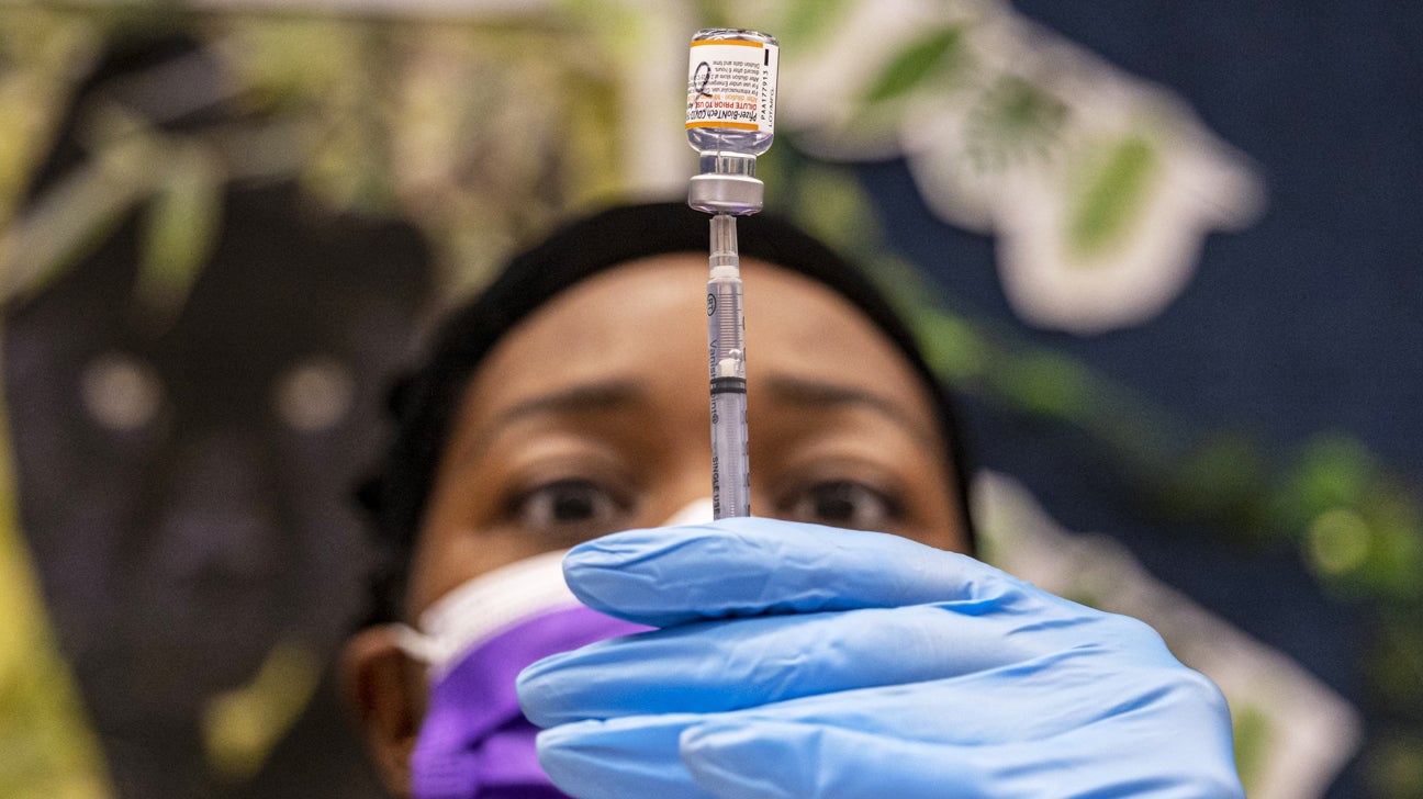 A female healthcare professional filling a needle with the fluid from a vial of a vaccine.