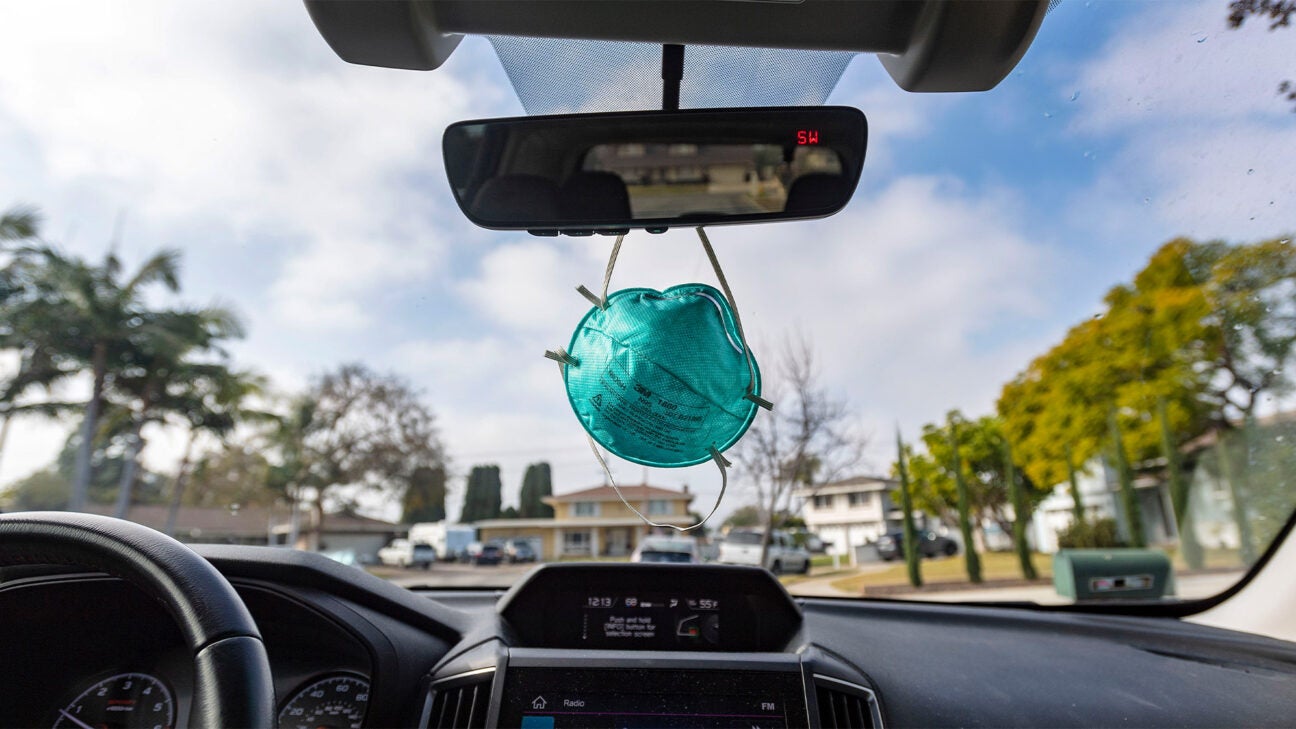 A mask hangs from a car's rear view mirror, ready when needed