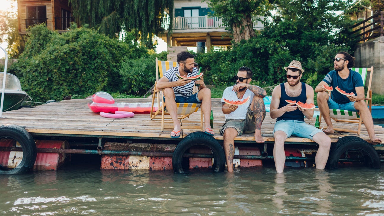 Four men eat watermelon while sitting on a dock