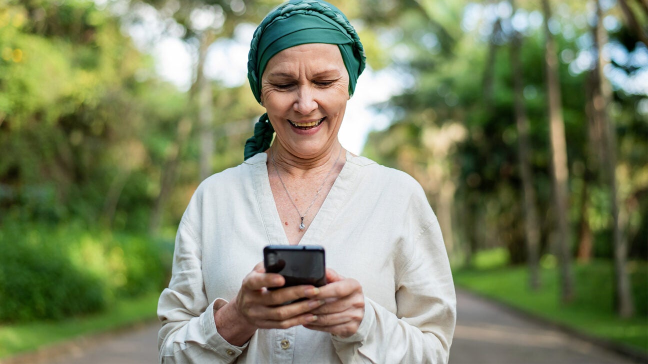 A woman wearing a green head scarf smiles as she looks at her cell phone