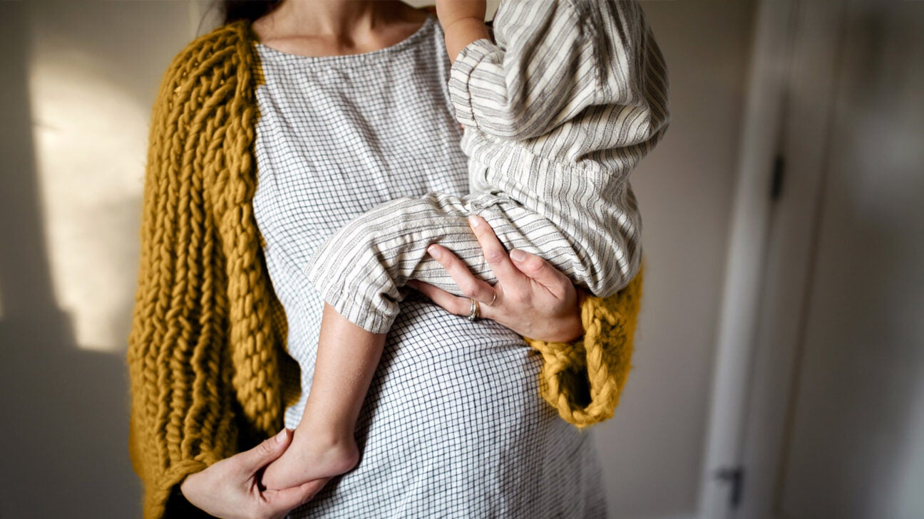 A pregnant woman wearing a shawl holds a young child