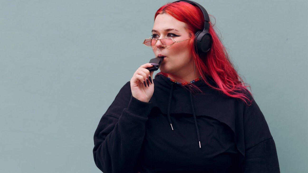 A young woman wearing headphones vapes