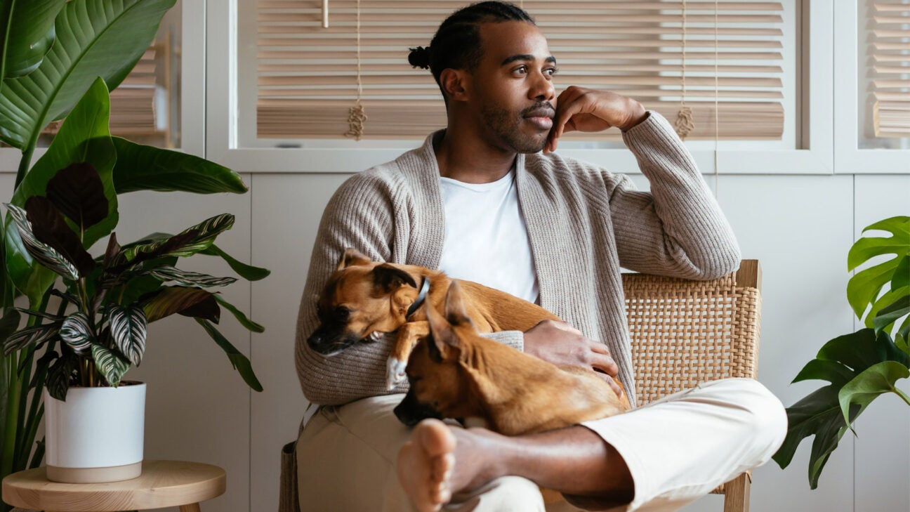 A man holds a dog in his lap as he sits in a room