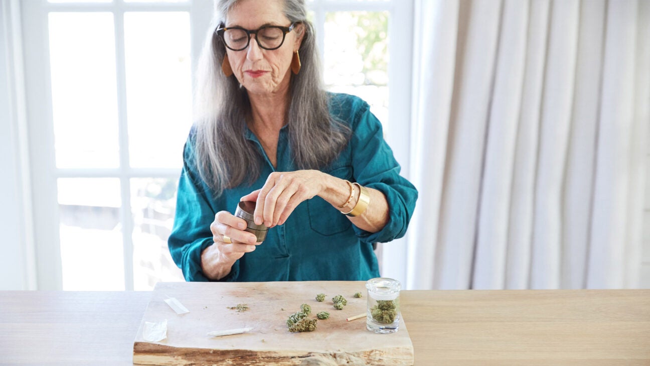 An older female rolls a joint with CBD flower on a table