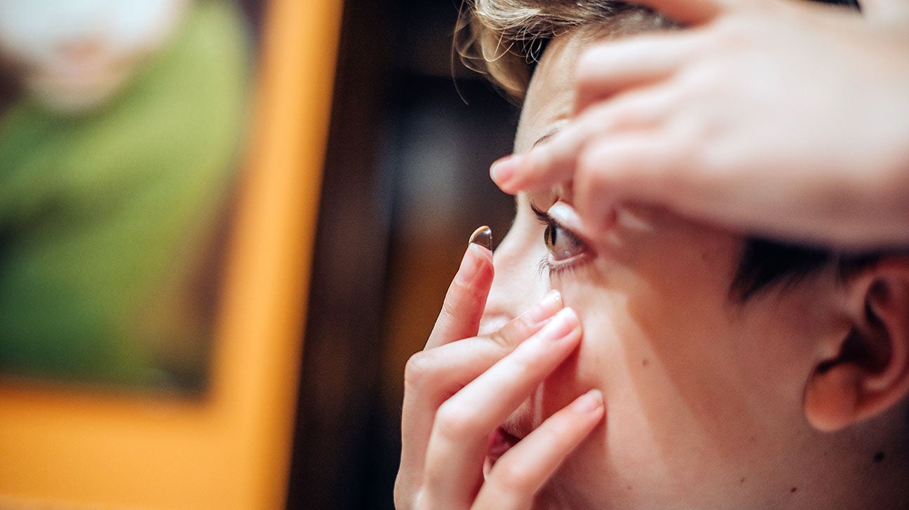 A woman carefully places a contact lens into her eye