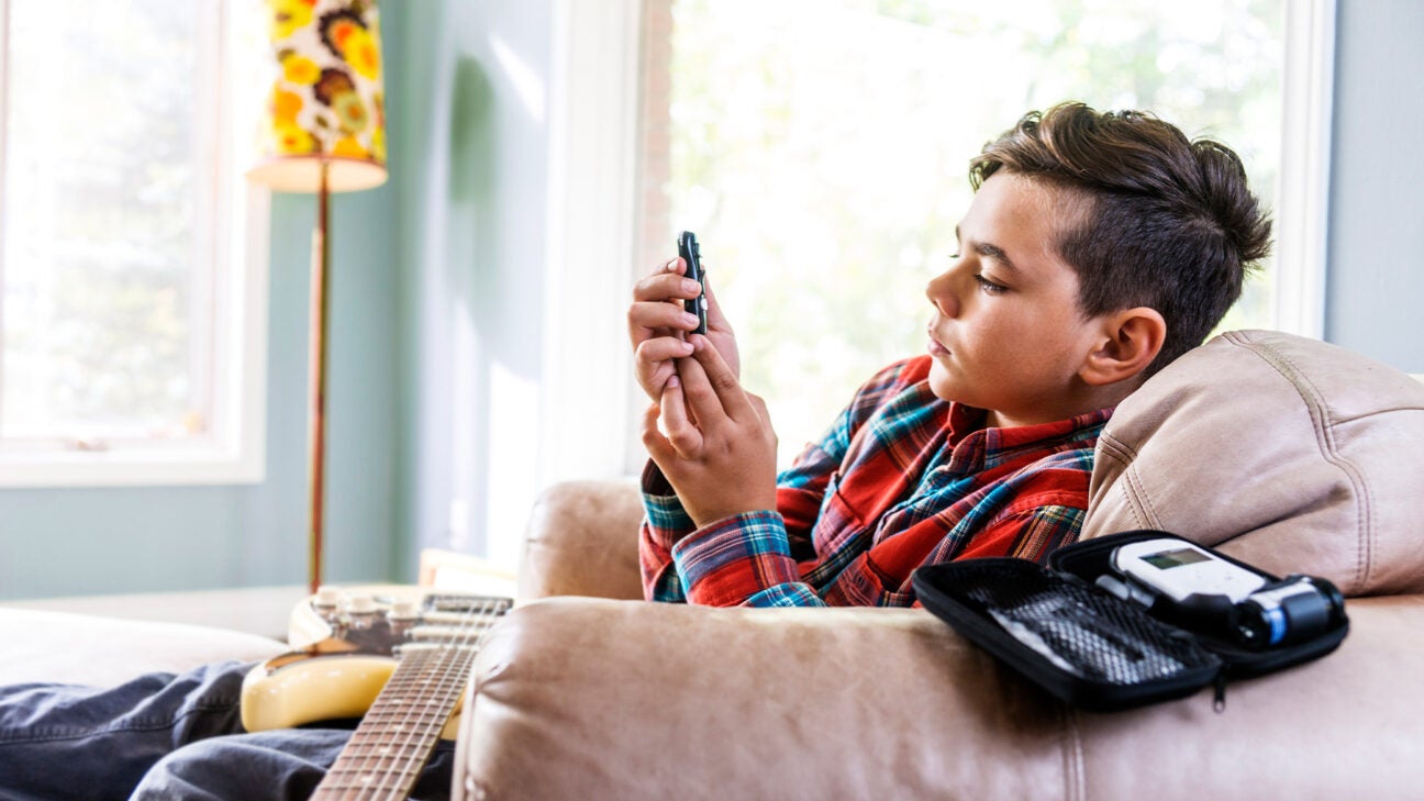 A teen boy in a family room checks his blood sugar levels while resting in an armchair