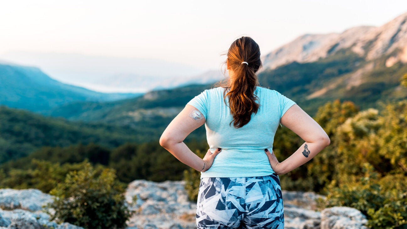 A female hike wearing a patch stands on a mountainside and looks out over a valley