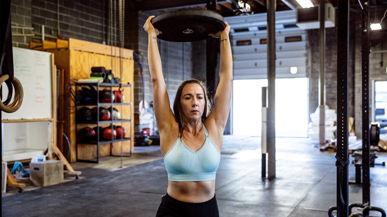 A younger woman lifts a weight over her head