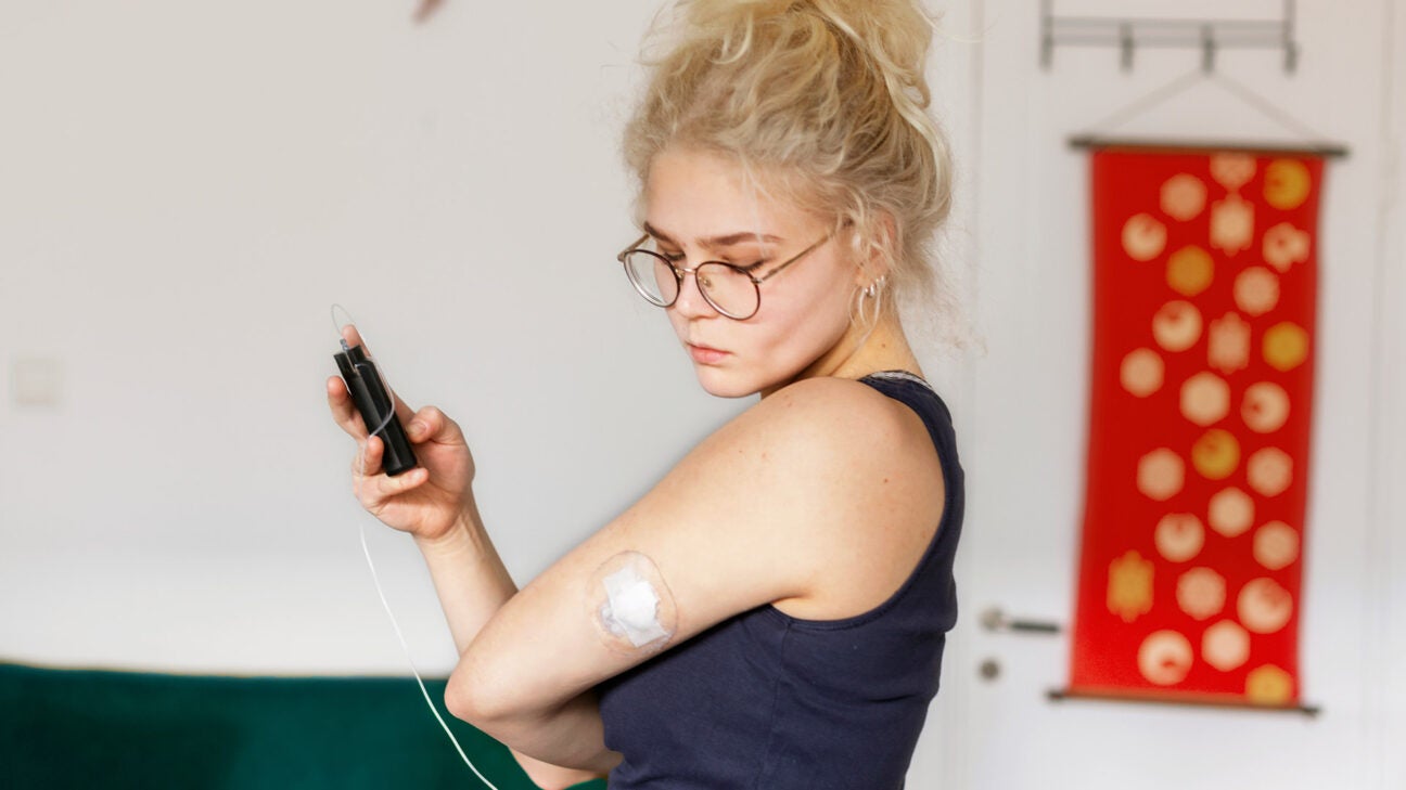 A younger woman checks an insulin patch on her left arm