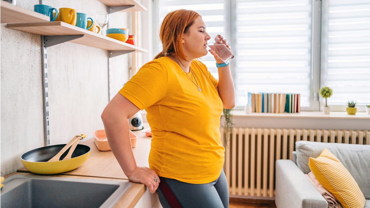 A woman drinks water in her kitchen.