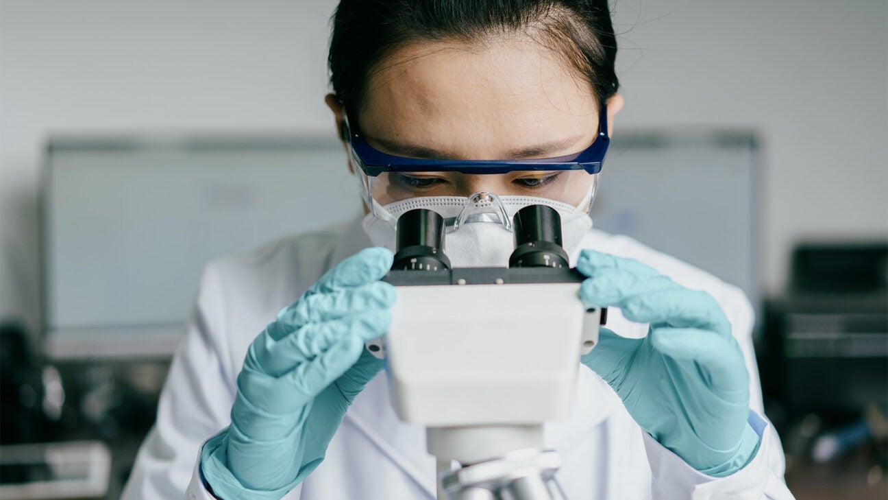 A female scientist in a lab peers into a microscope