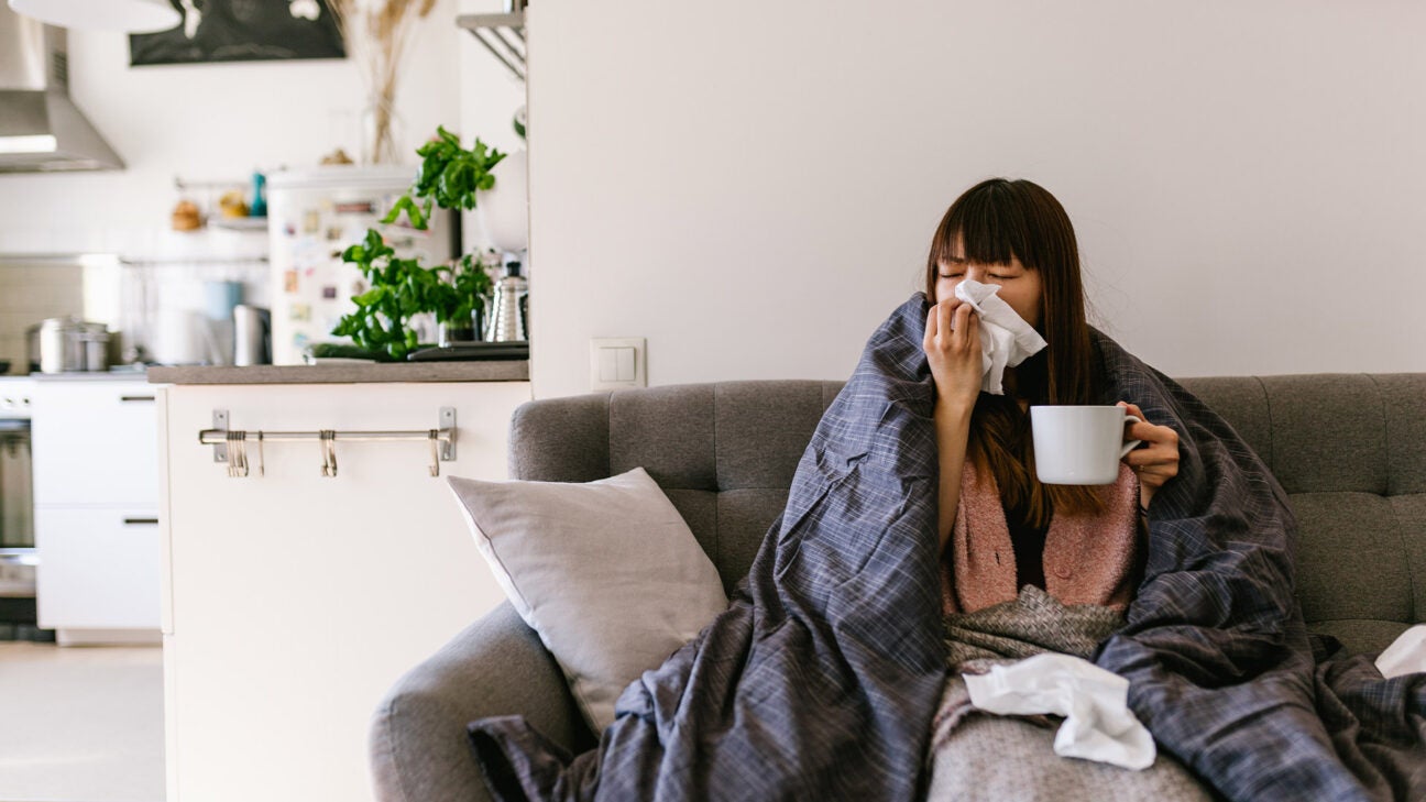 A woman with the flu sits on a sofa.