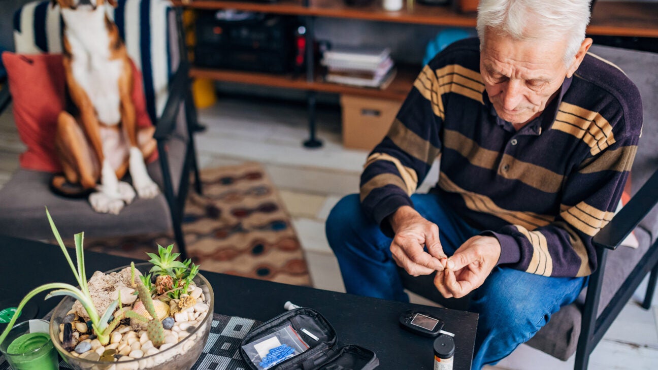 An older man sitting in a den pricks his finger to check his blood sugar levels