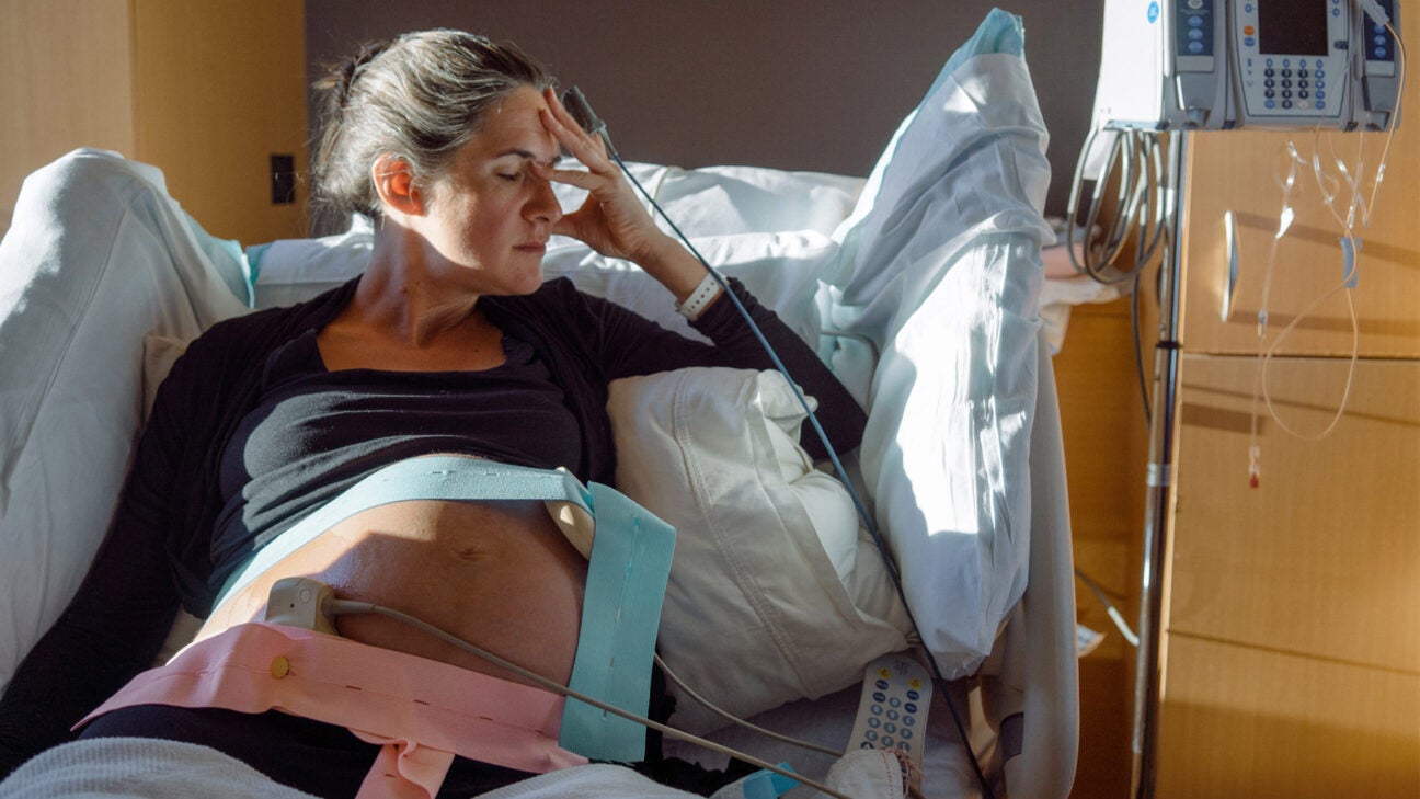 A pregnant closes her eyes and holds her head while laying in a hospital bed