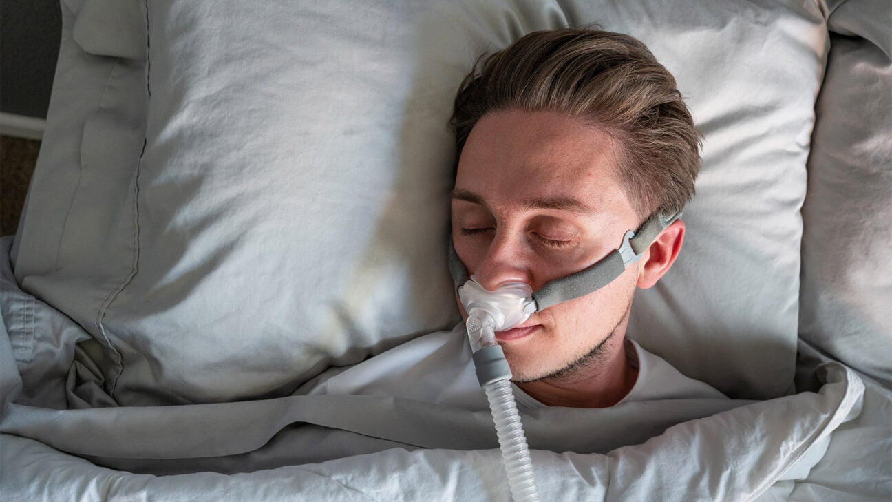 A younger man sleeps comfortably with a sleep apnea device attached to his nose