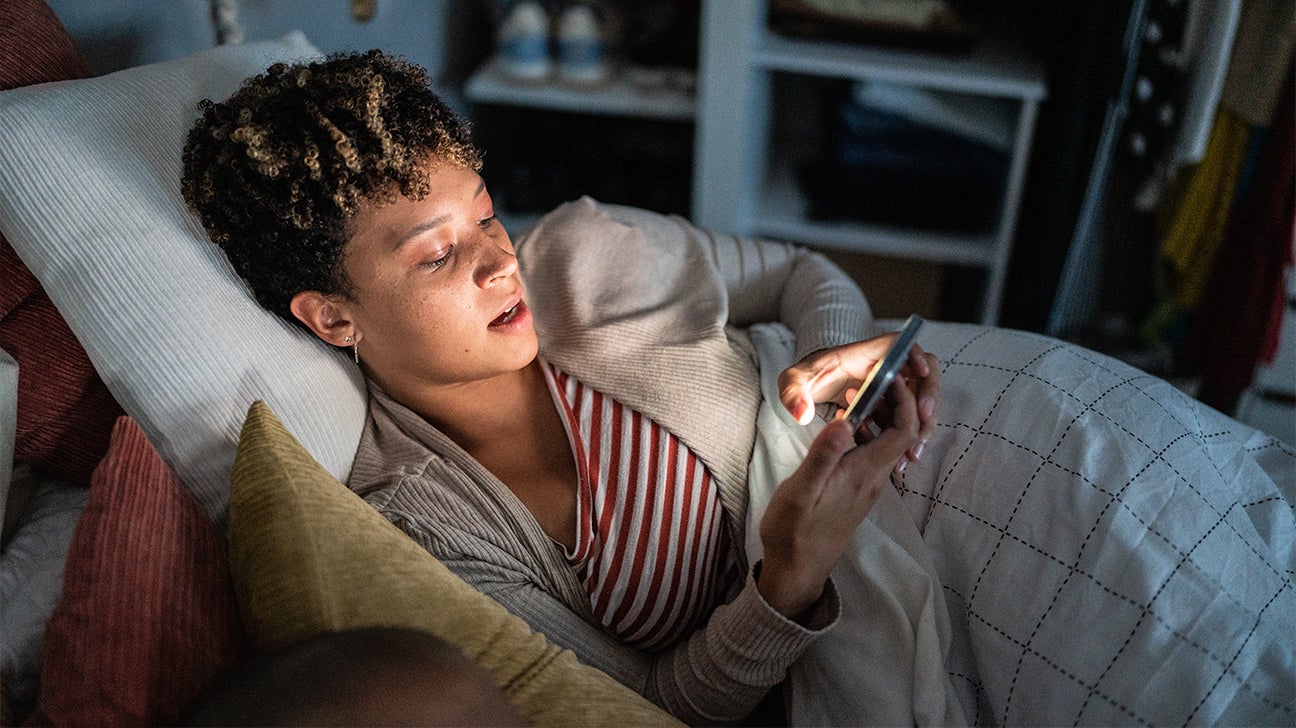 woman lying in bed looking at smart phone
