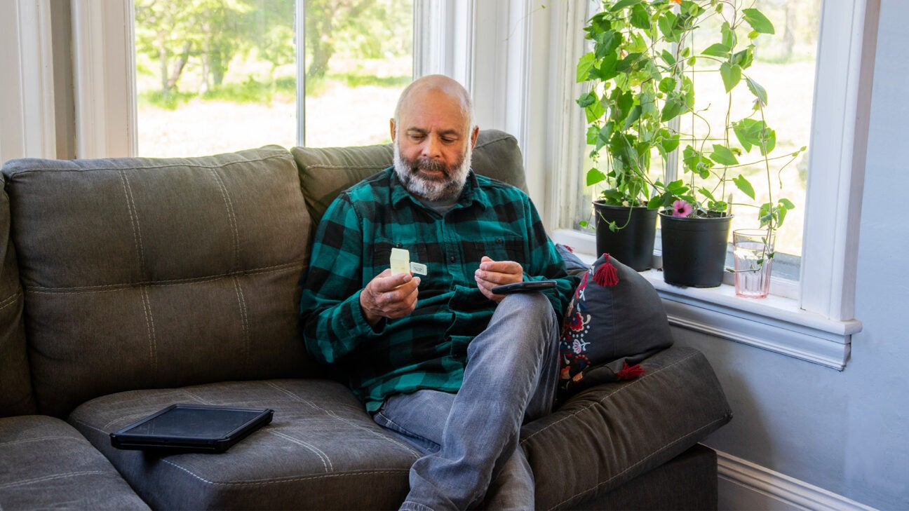 An older man sitting on a couch in his front room looks at a pill bottle