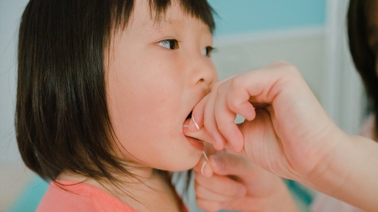 A dental assistant flosses the teeth of a young girl