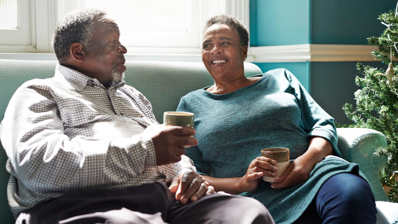 An older man and woman drink coffee while sitting on a couch