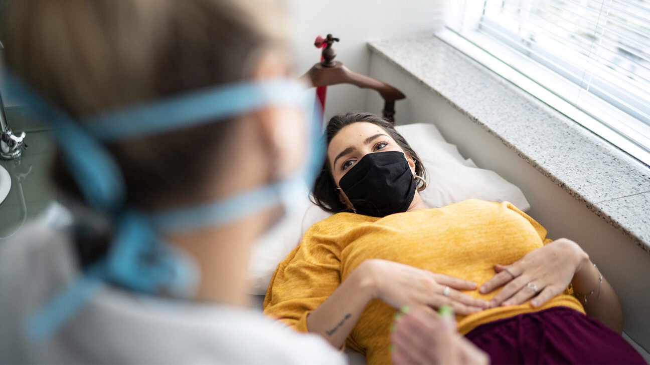 A female doctor speaks with a young woman resting on a bed while holding her stomach