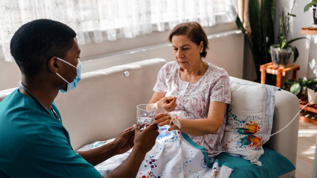 An older woman receives a pill and a glass of water from a nurse