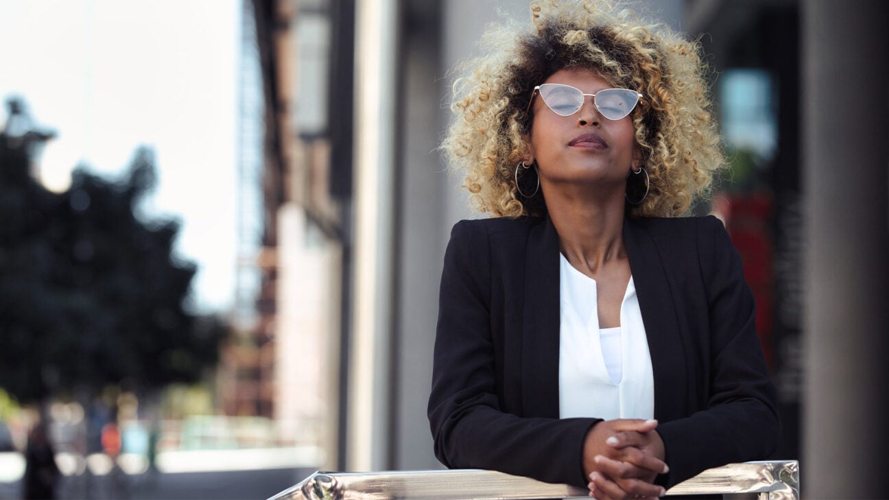 A woman closes her eyes as she enjoys some sunshine outside an office building