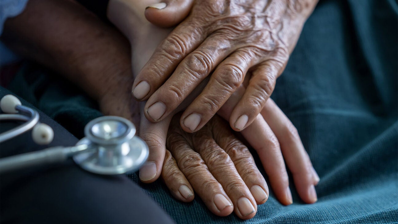 Three clasped hands rest on a bed near a stethoscope