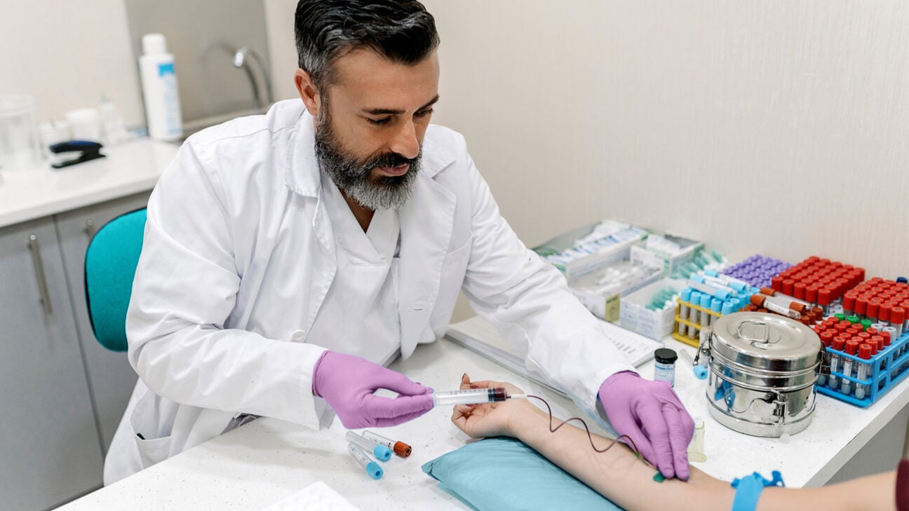 A medical professional takes a blood sample from the arm of a man