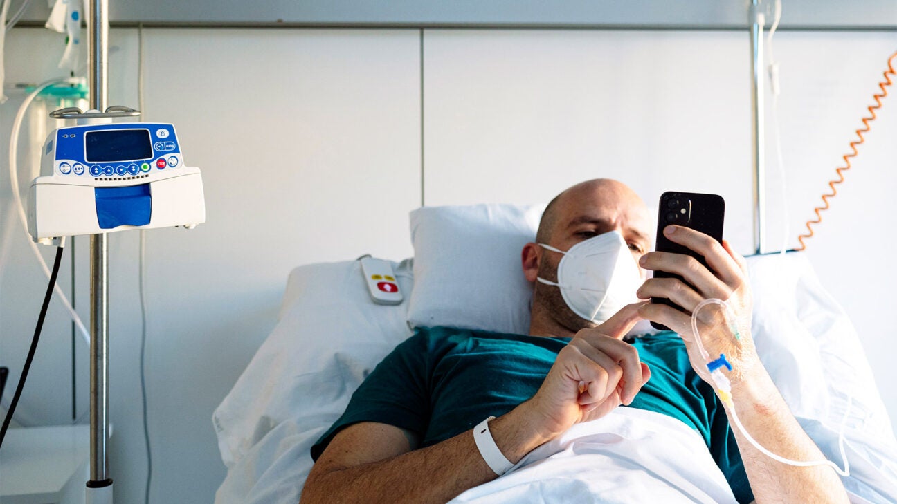 A Millennial male lies in a hospital bed wearing a mask