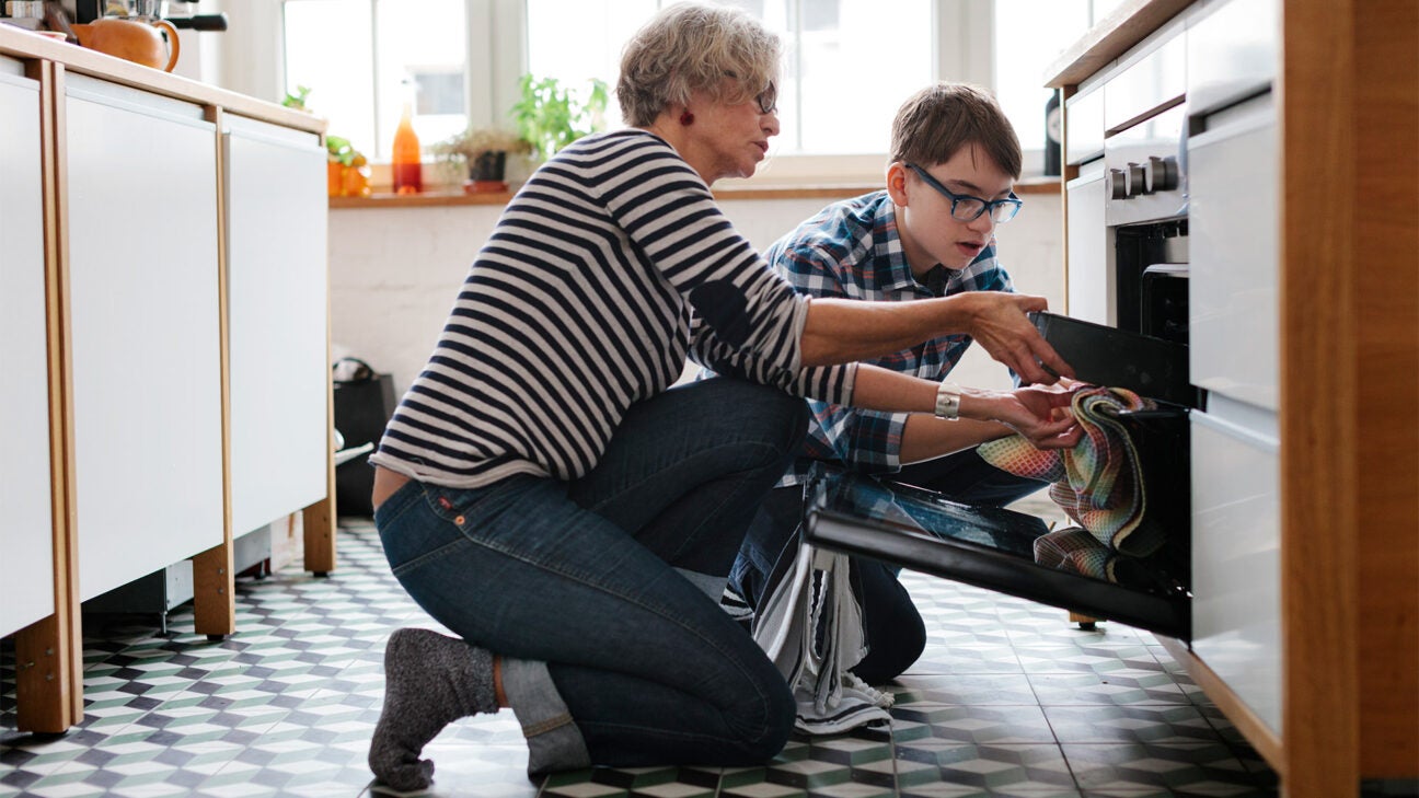 A mother and teen son lift a pan from inside an oven