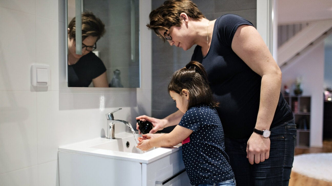 A parent helps their child wash their hands.