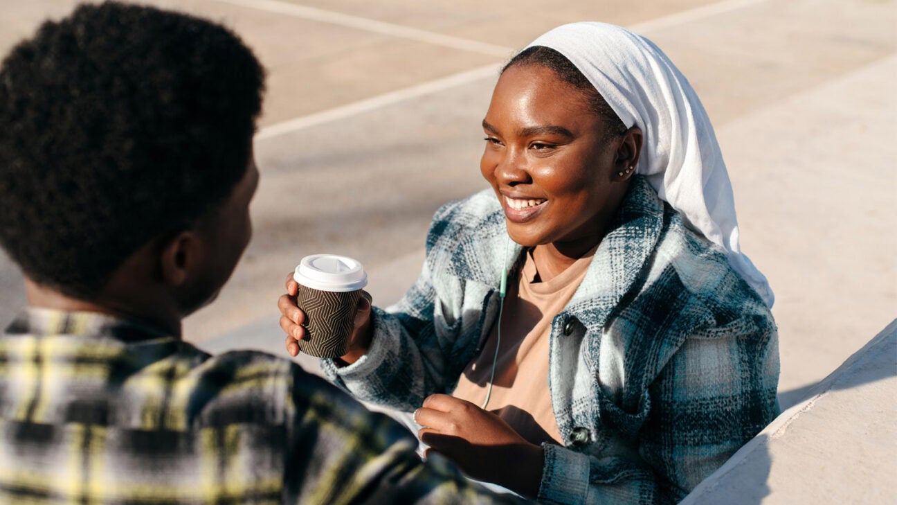 A woman holding a coffee is seen in a conversation.