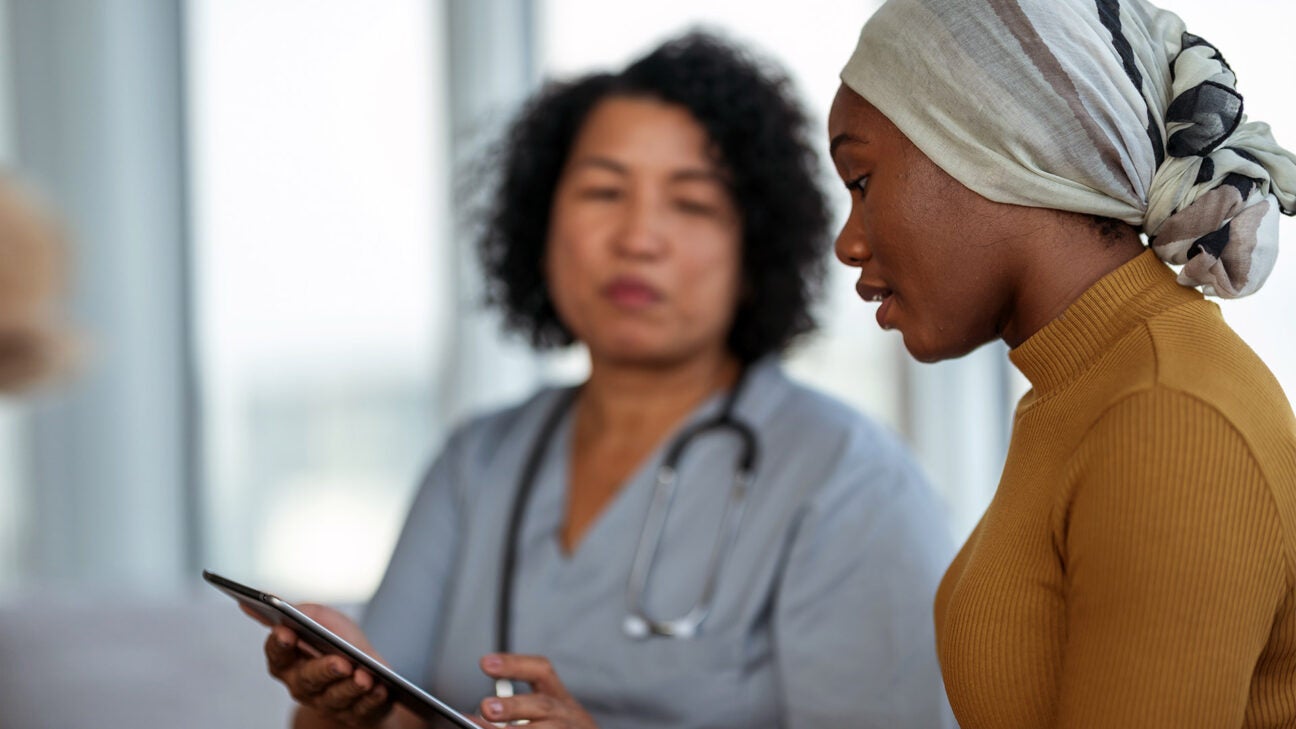 A younger woman wearing a scarf speaks with a healthcare professional