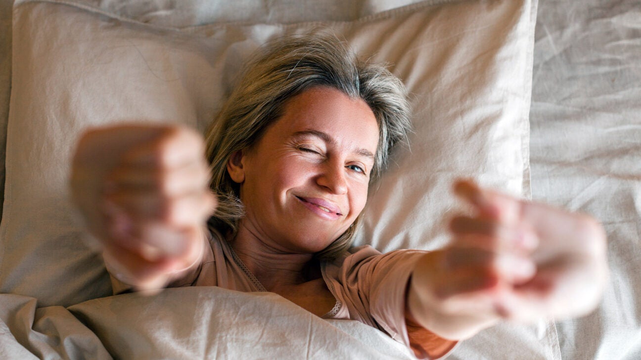 A woman stretches in bed while waking up