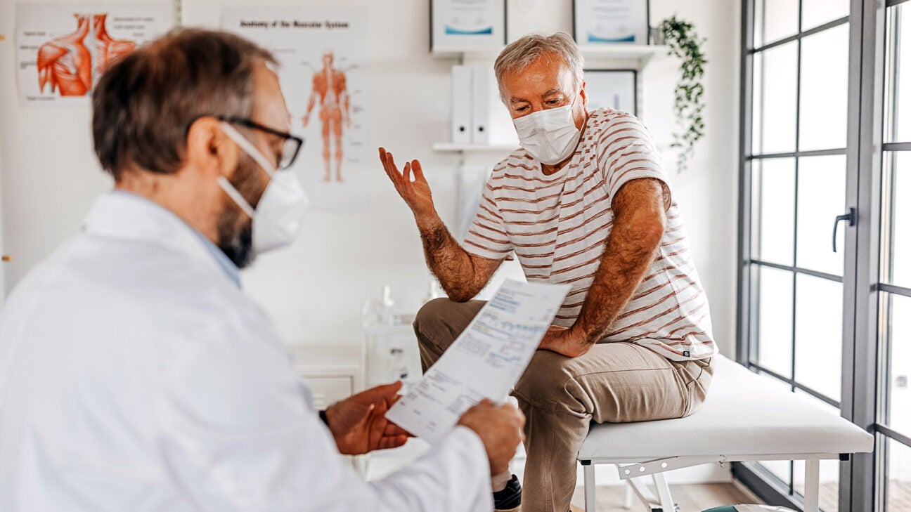 An older man speaks with a physician while sitting on an exam table in a doctor's office