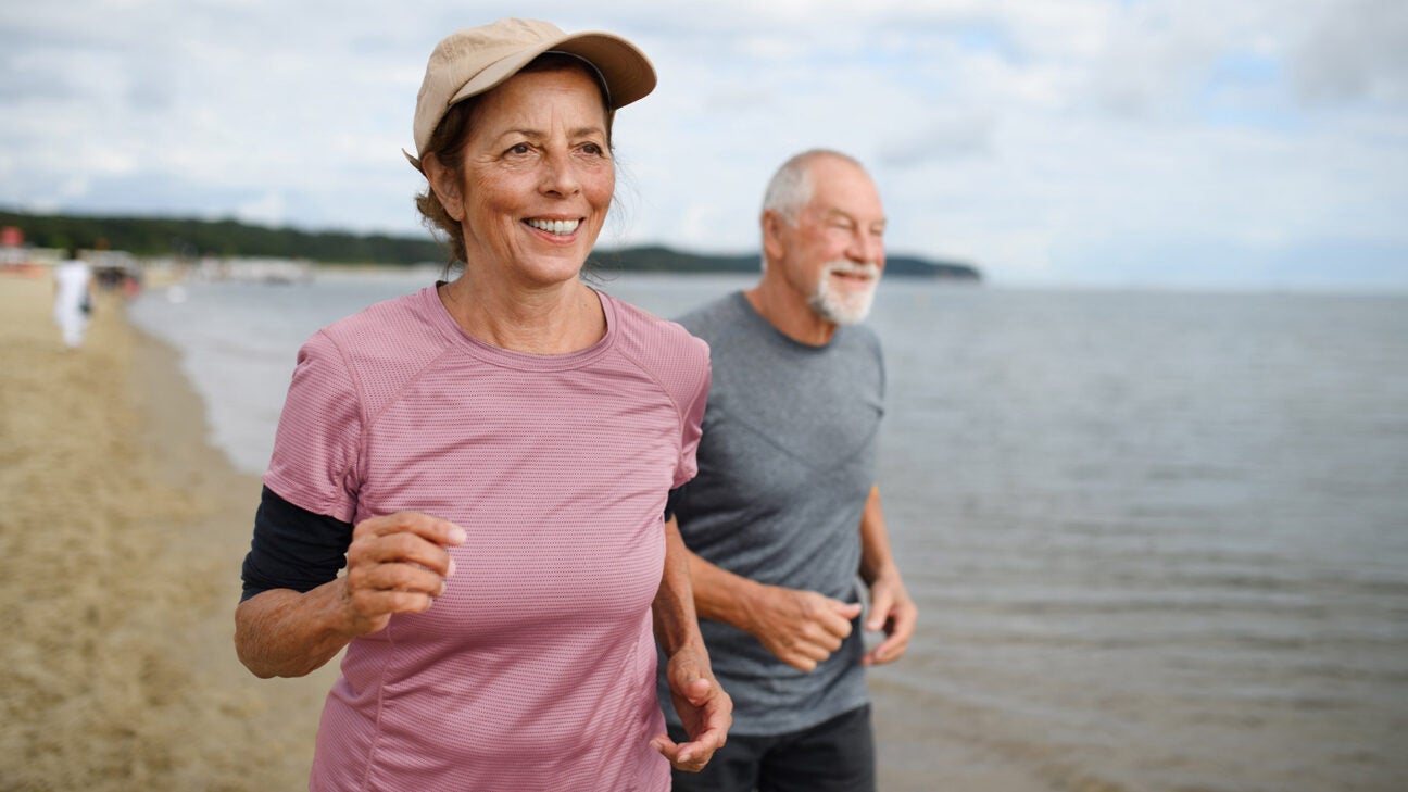 An older woman and man run along a beach