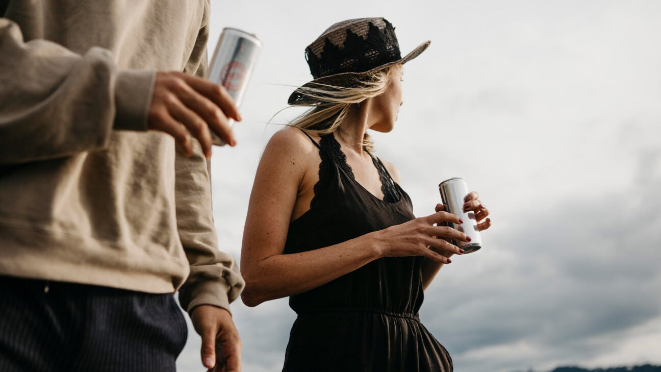 Two people drinking from soda cans outdoors. 