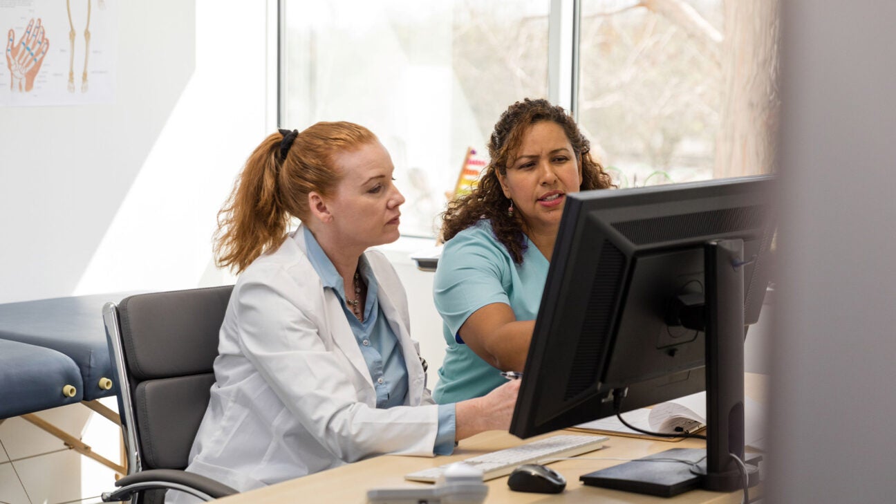 A physician talks to a patient at a desk.