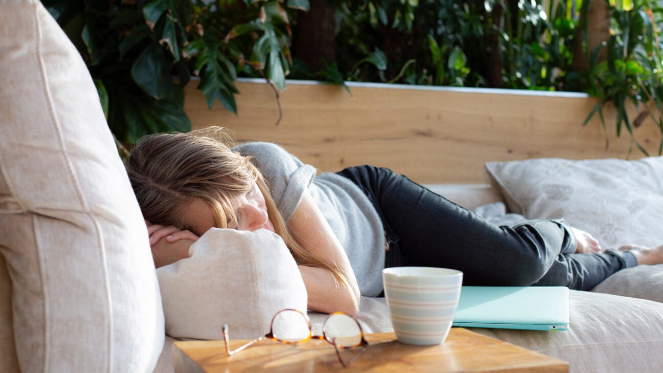 A woman naps on a couch on a deck outside