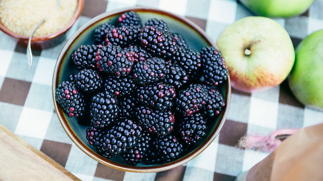 A bowl of blackberries on a table with apples. 