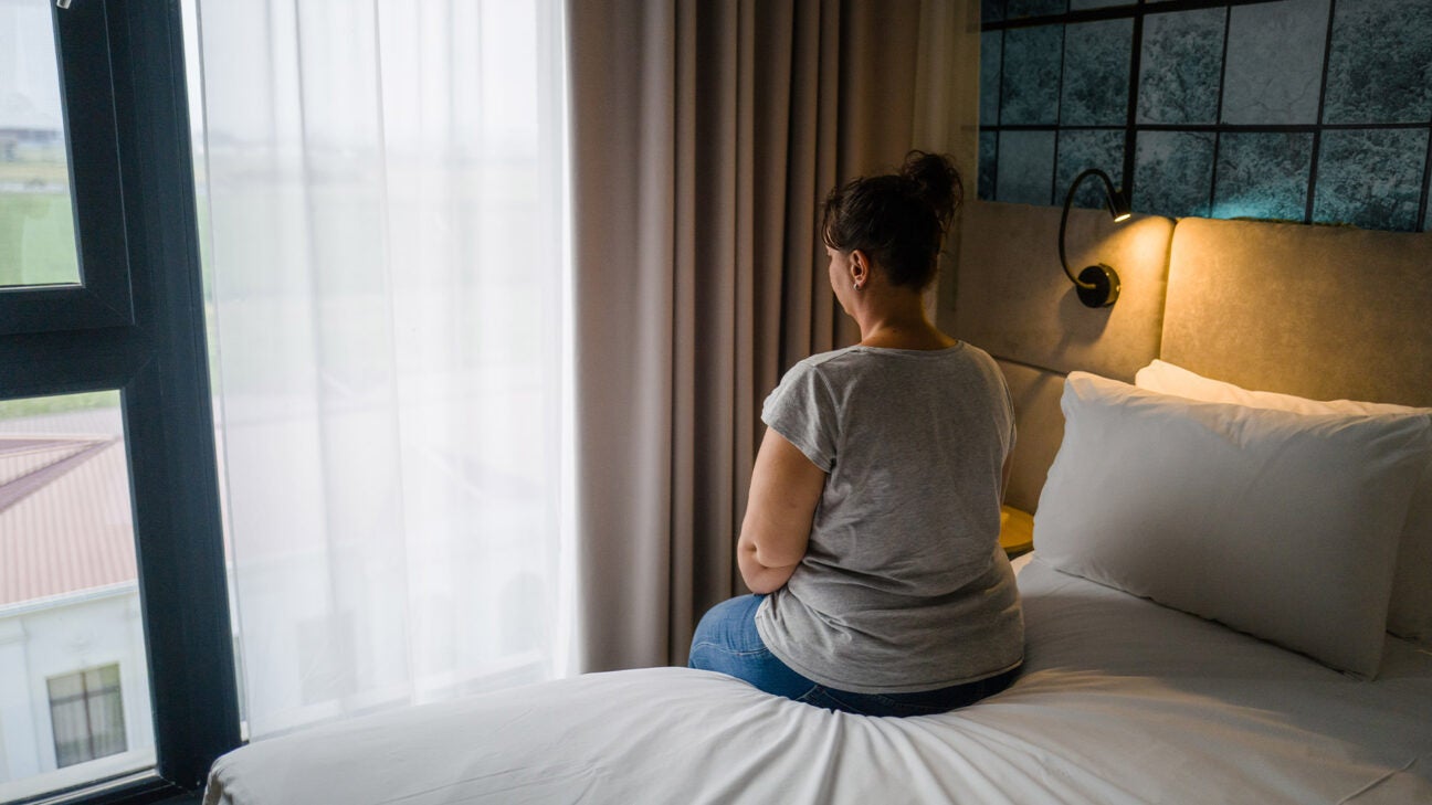 A woman sitting on a bed looking out a window.