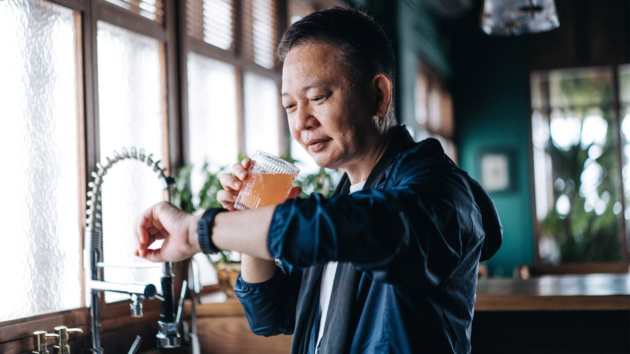 A man checks his watch while holding a drink.