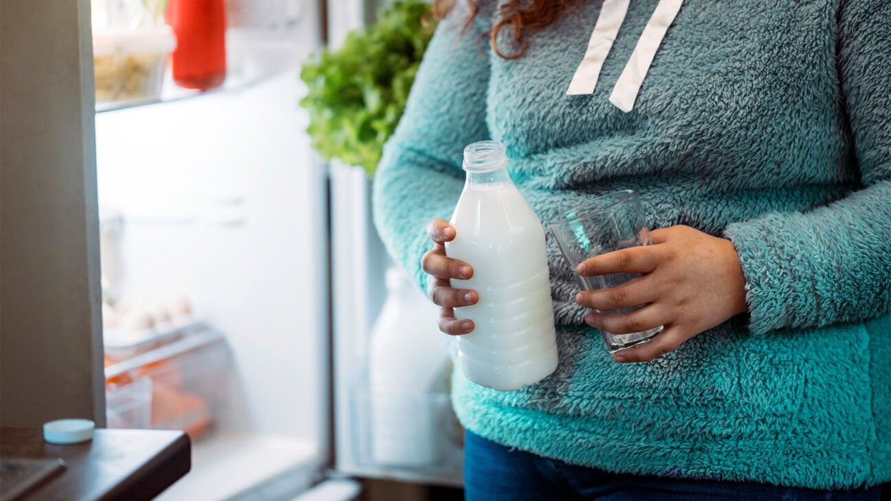 A person holding a bottle of milk and a glass.