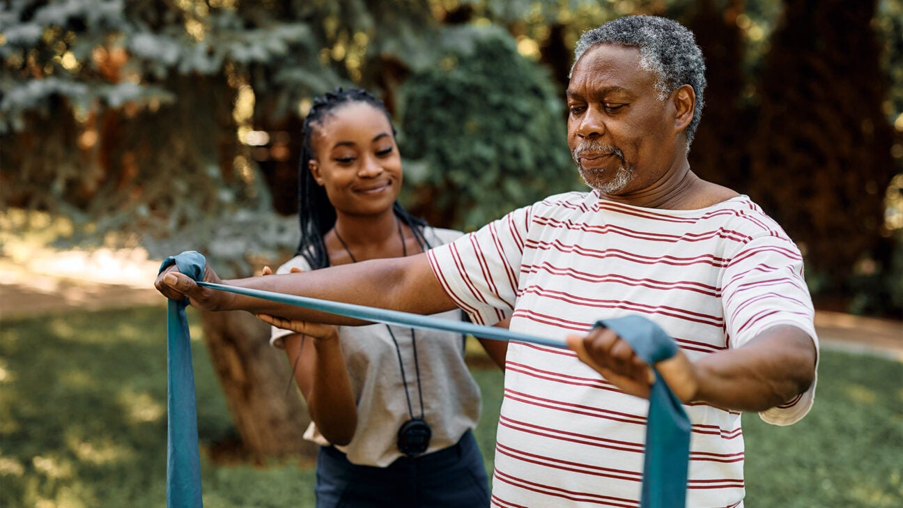 A woman helps a man with an exercise band.