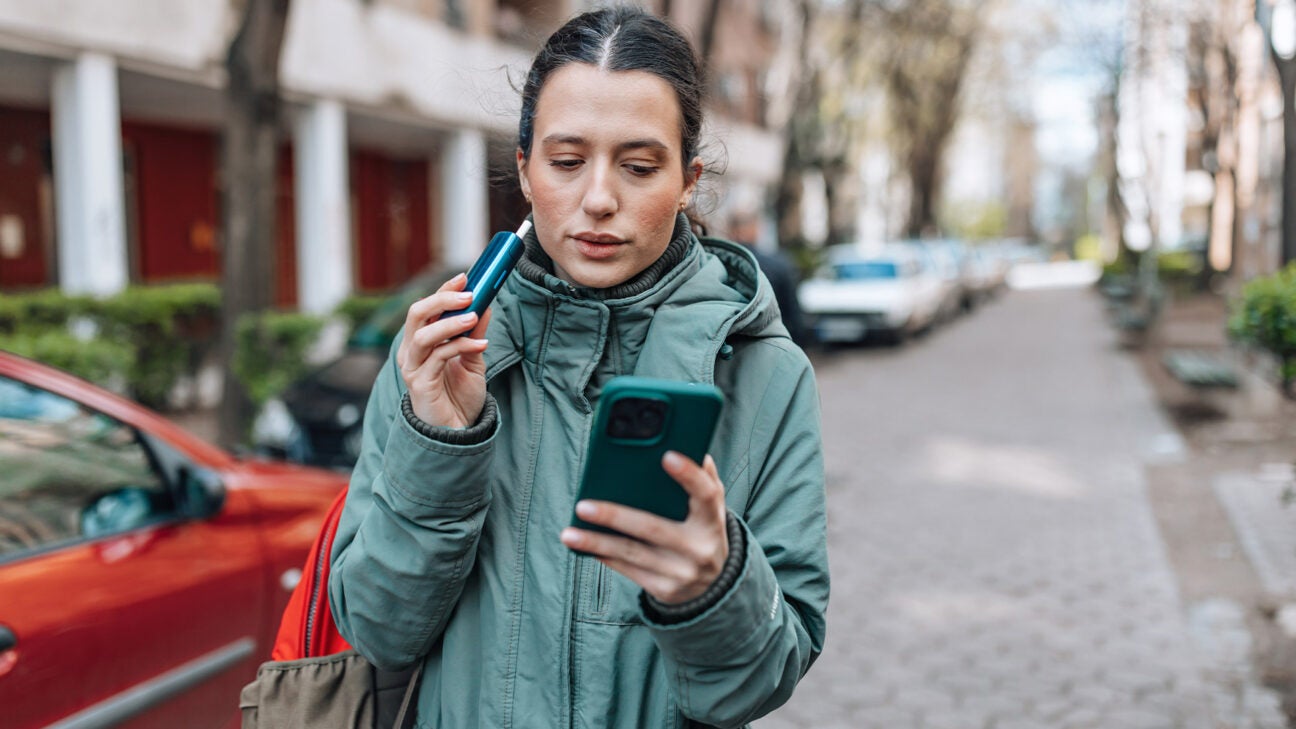 A woman vaping while looking at a smart phone.