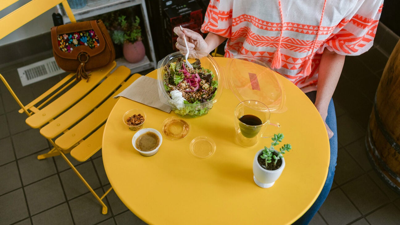 A person eats a salad on a yellow table.