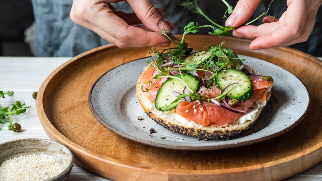 A person prepares a dish with salmon and vegetables.