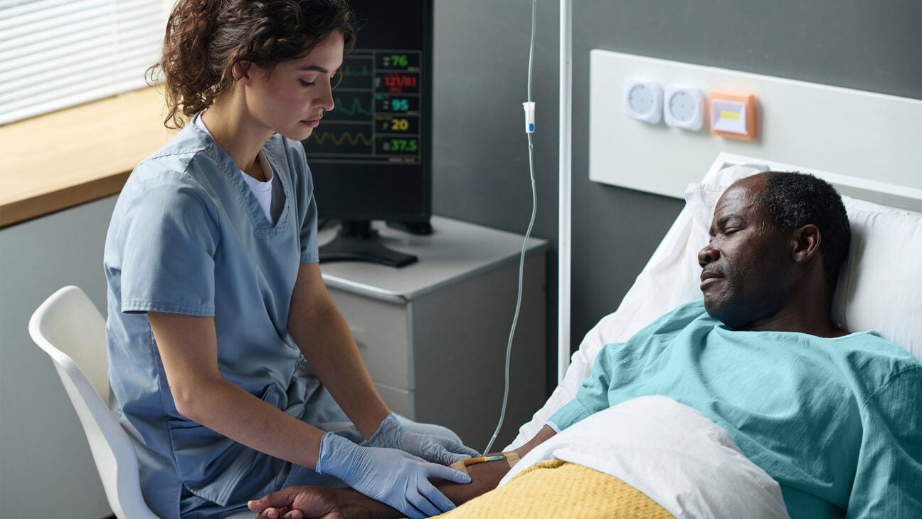 A healthcare worker treats a male patient in a hospital bed.